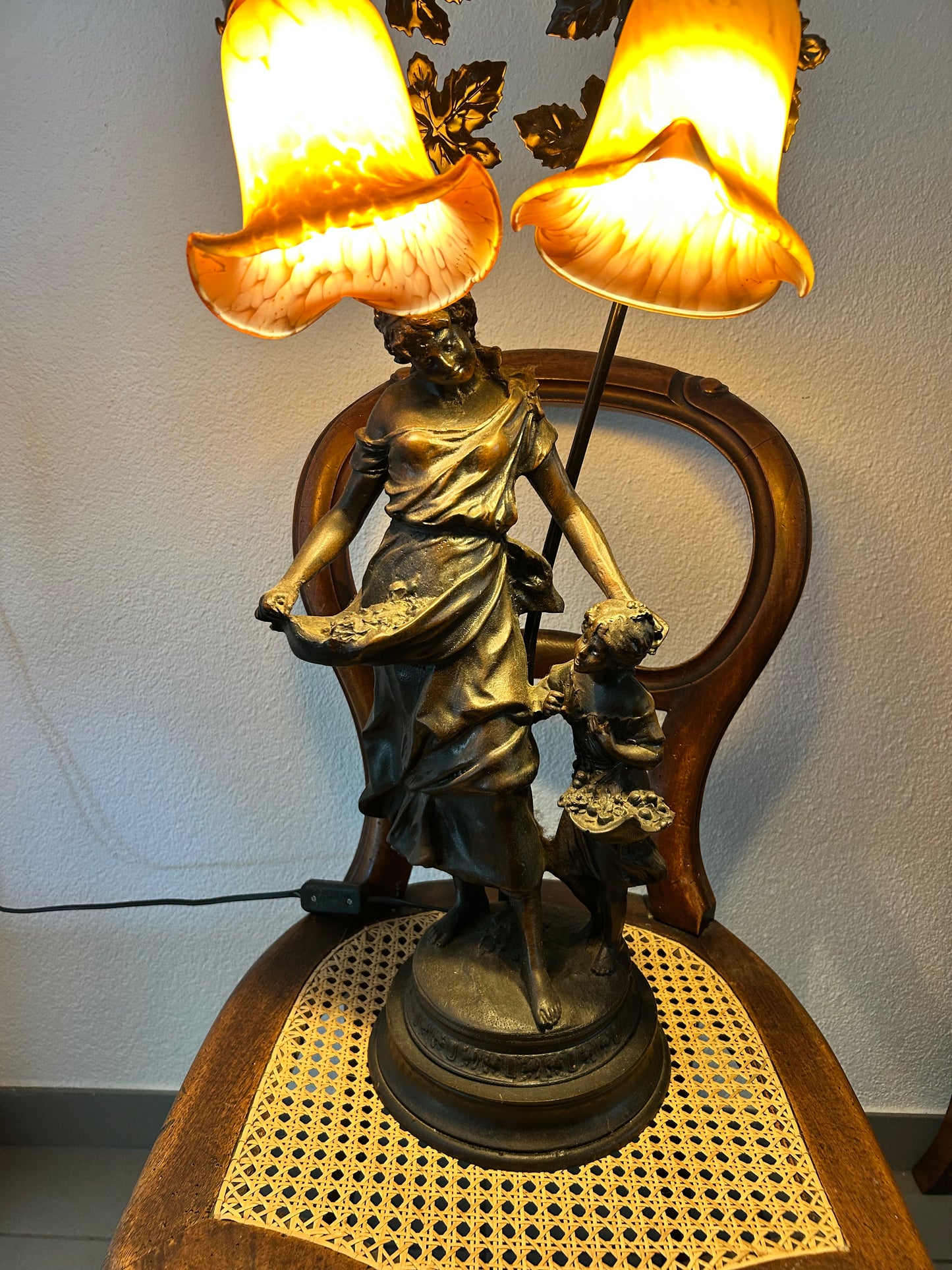Full view of figural lamp lit, woman and child spelter figures with golden light
